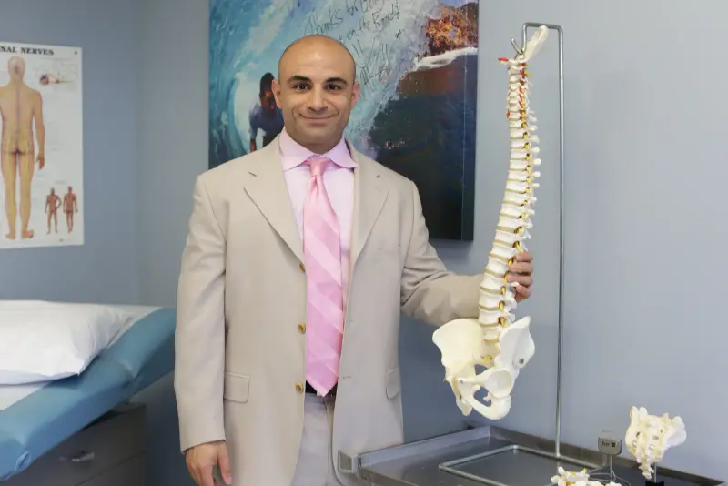 Dr. Hooman Melamed reviewing spinal anatomy on a model in his exam room